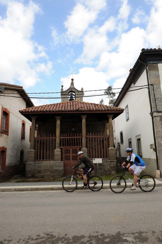 Dos ciclistas pasan por delante de la capilla del Santo Cristo en La Pola