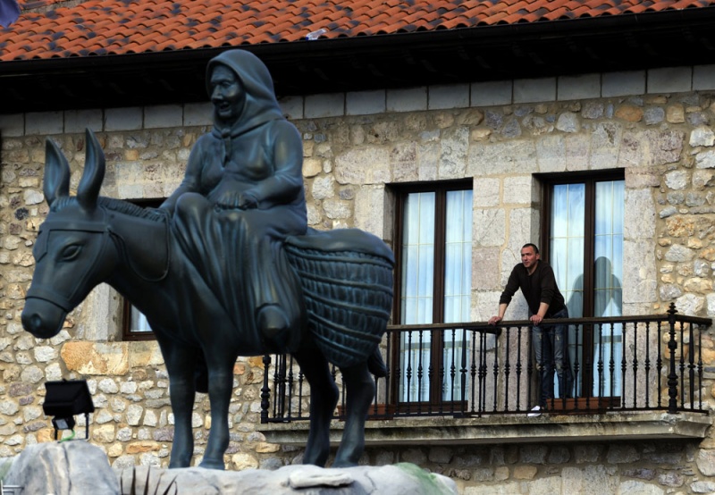 Un hombre se asoma al balcón del hotel María Manuela, mirando a la estatua que recuerda a la madre del propietario sobre la yegua que utilizaba para bajar los domingos a Cangas de Onís a vender los productos que elaboraba en Llenín, su pueblo