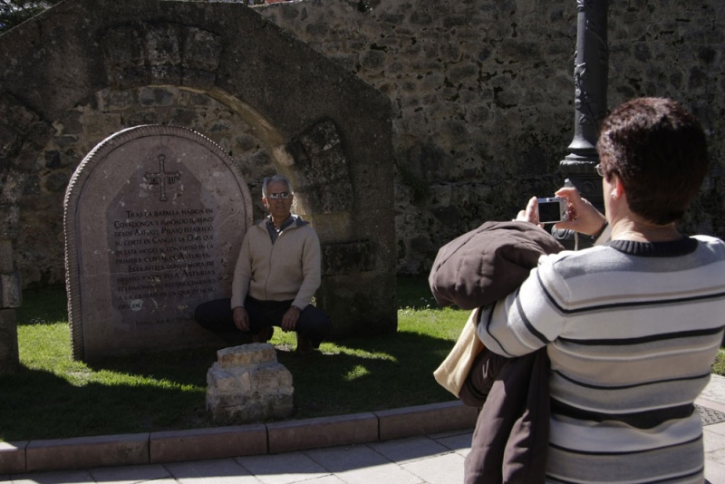 Un hombre se fotografía ante la estela que atestigua la antigüedad del Puente Romano y cuenta parte de la historia del reino de Asturias.