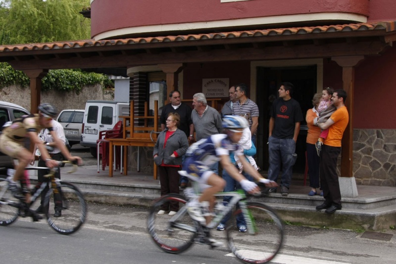 Varias personas observan el paso de la Vuelta Ciclista a Asturias ante el bar Casa Carlos.